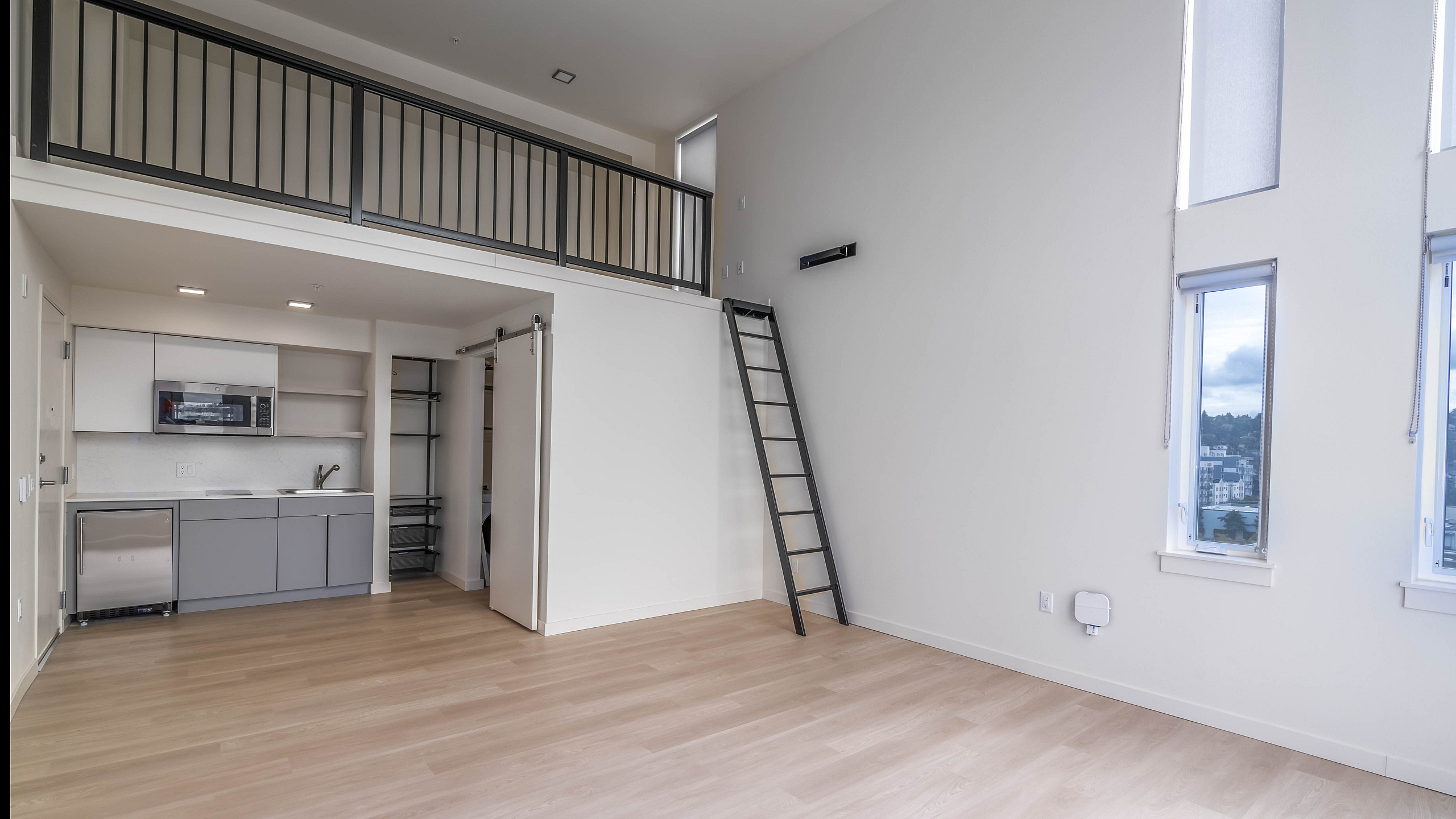 Modern apartment with an open loft design, featuring a sleek kitchen, light wood floors, and large windows offering abundant natural light.