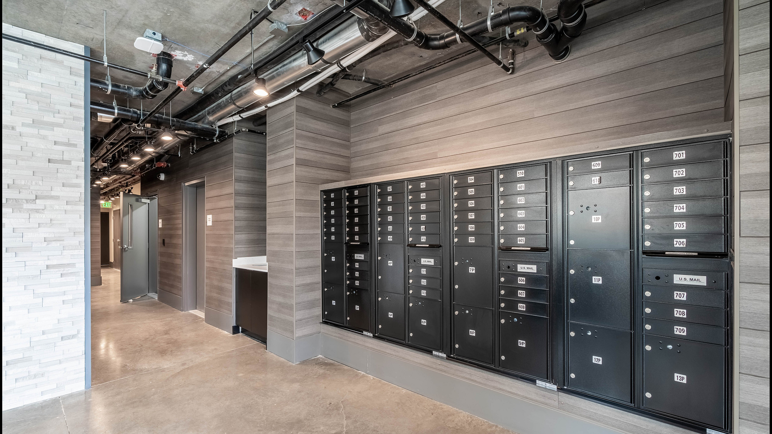 Modern apartment mailroom with sleek locker design and industrial-style ceiling.