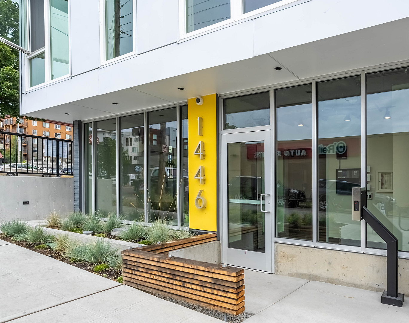 Contemporary building entrance with sleek glass doors and vibrant yellow accent, offering a modern and inviting look.