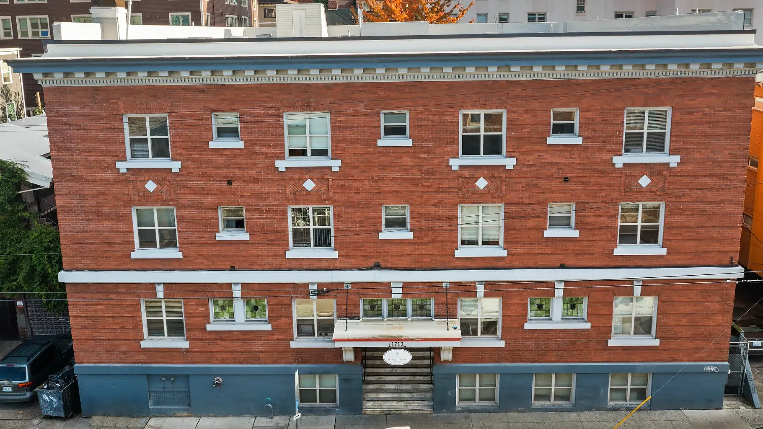 Charming red-brick apartment building with multiple windows, ample parking, and urban street view.