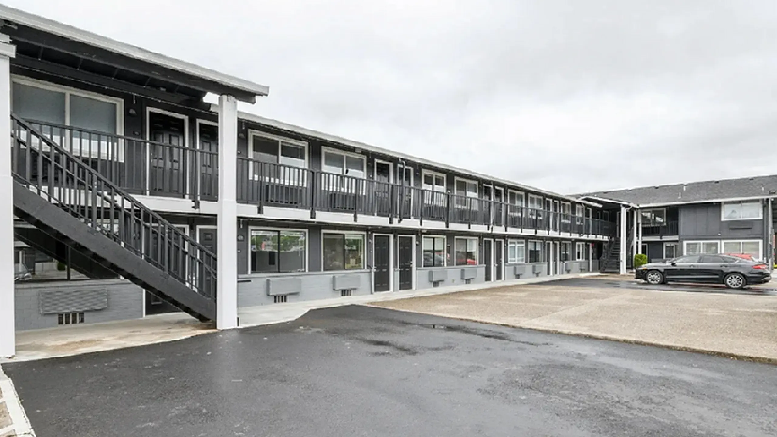 Modern two-story apartment complex with sleek gray exterior, spacious parking area, and inviting balconies.