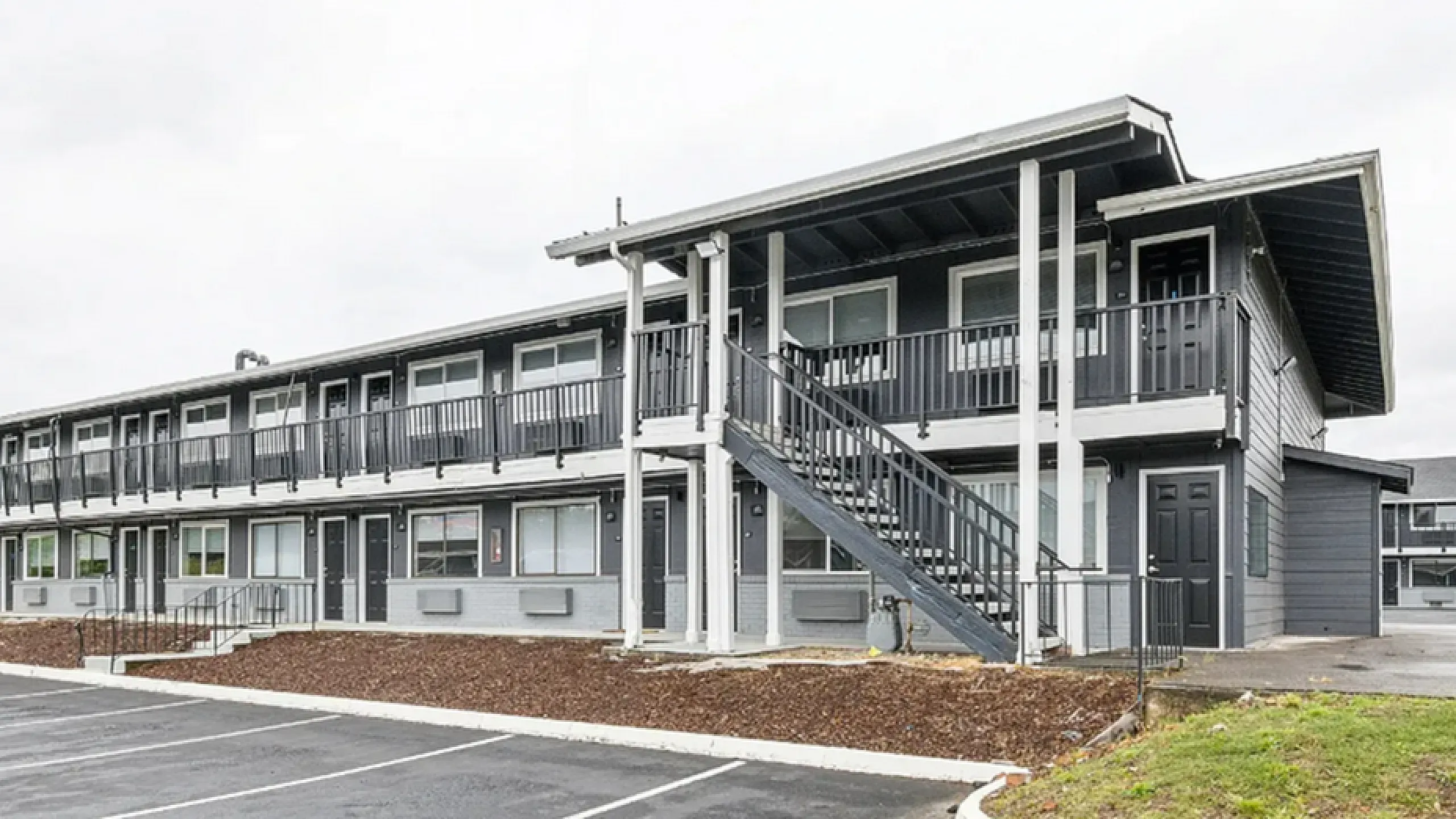 Modern two-story apartment building with balconies, sleek design, and convenient outdoor stair access, surrounded by fresh landscaping.