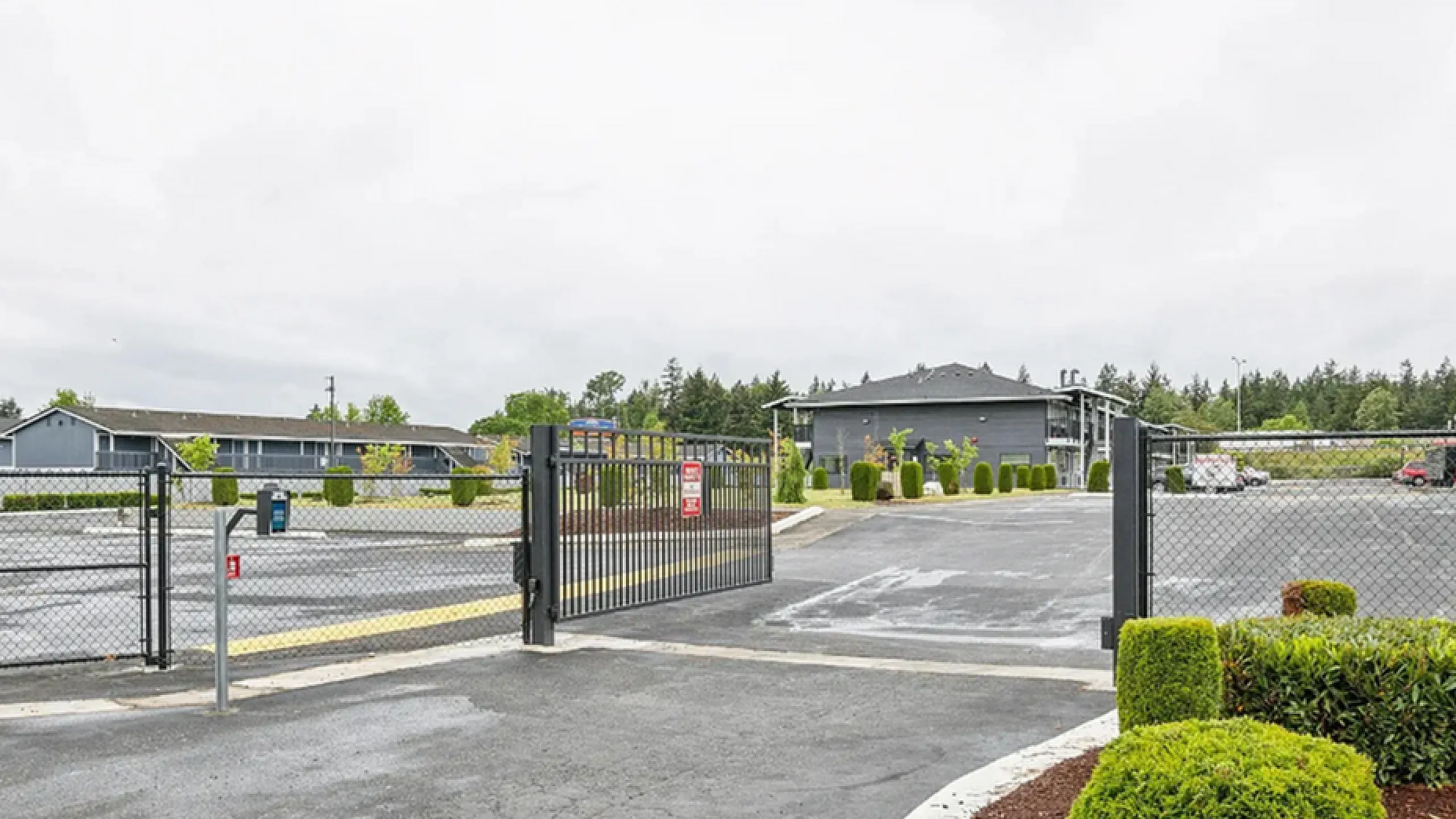 Inviting gated entrance to a modern apartment complex with lush landscaping and ample parking space.