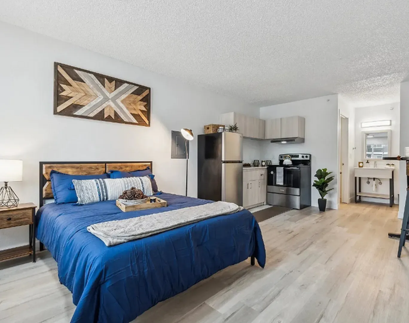Cozy studio apartment with modern decor, featuring a plush blue bed, compact kitchen, and stylish breakfast bar.