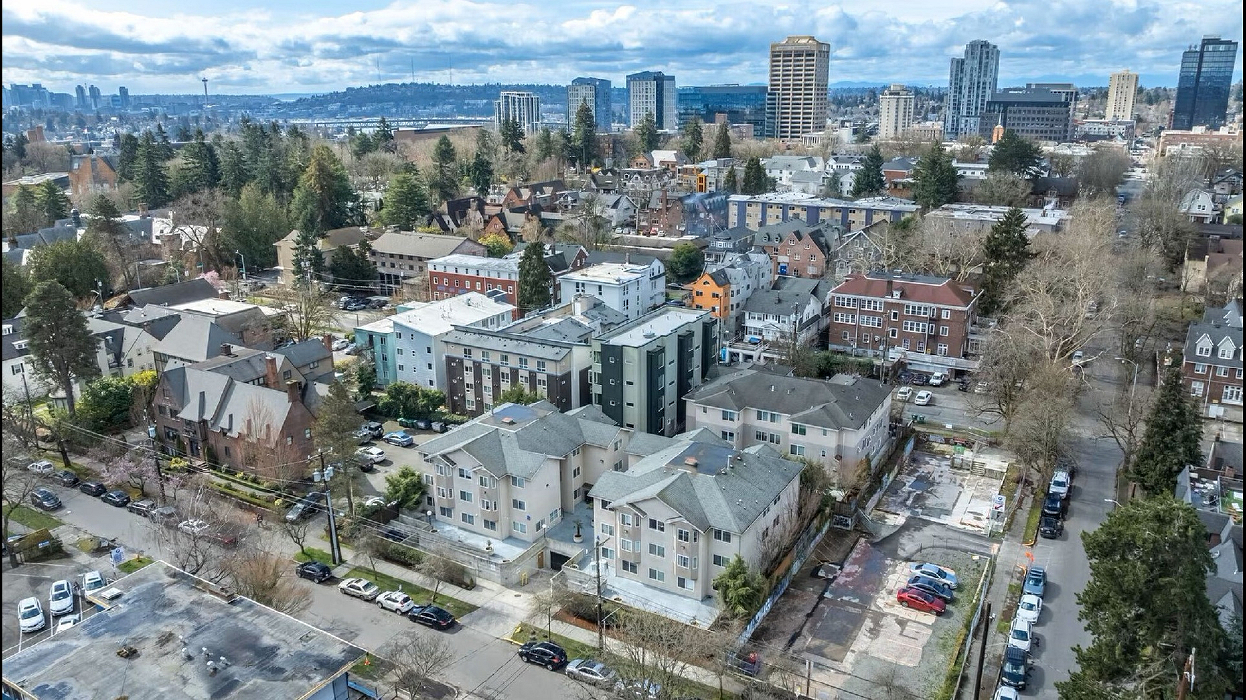 Vibrant aerial view of a bustling urban neighborhood with modern apartment buildings, lush greenery, and a dynamic city skyline nestled against a picturesque hillside.