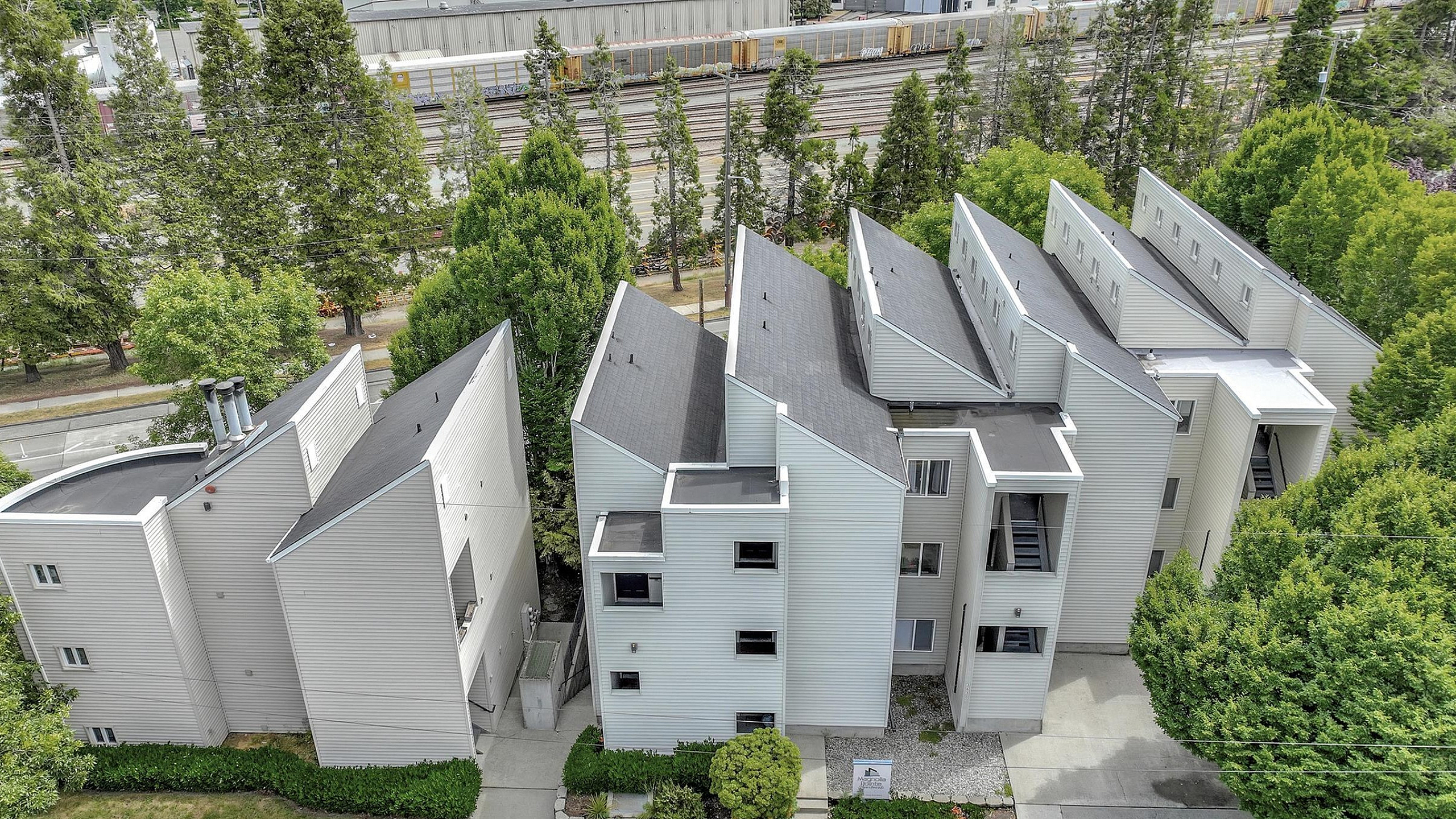 Modern multi-residential complex with distinct architectural design, surrounded by lush greenery and cityscape views.