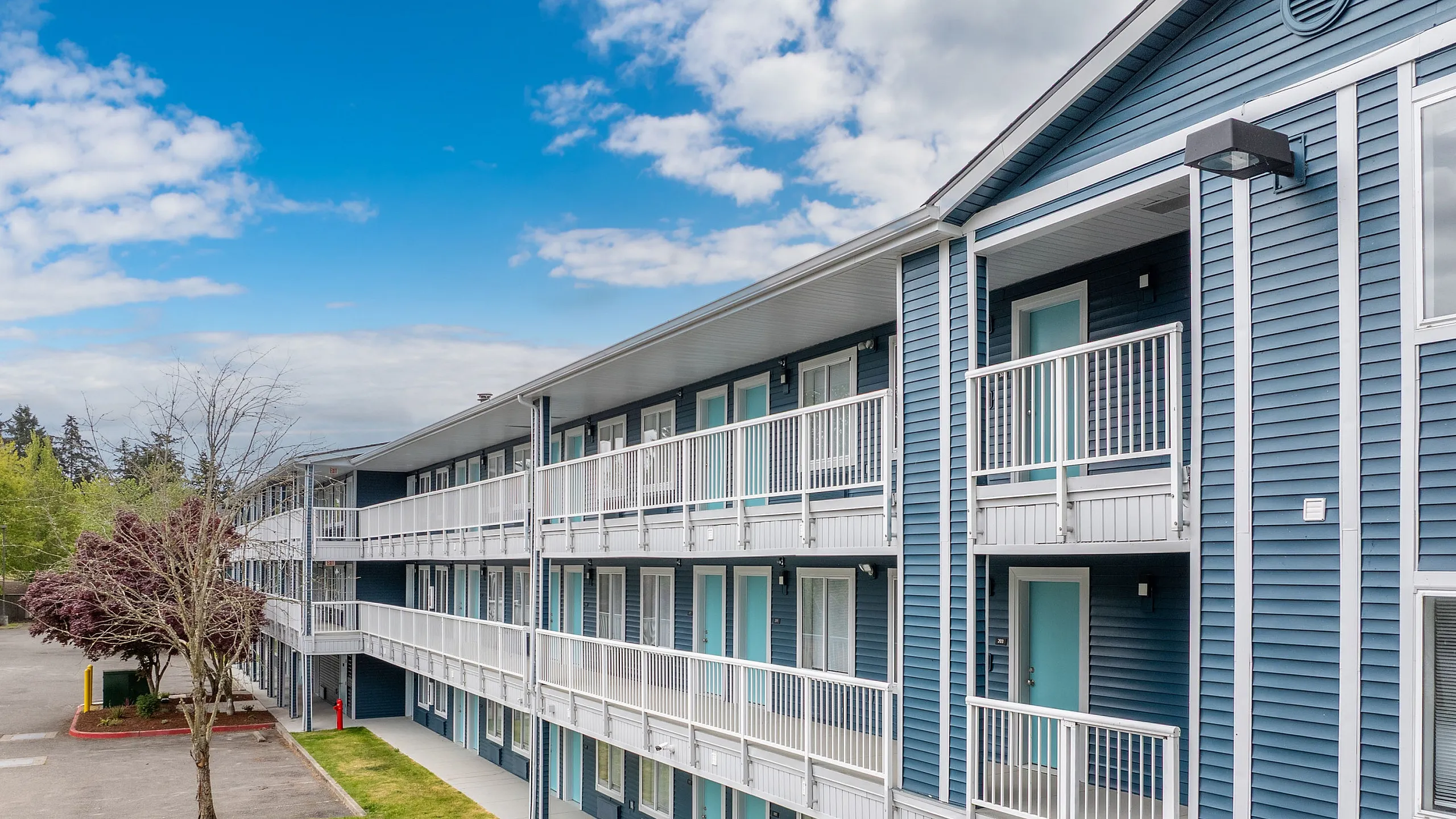 Charming apartment building with modern blue exterior and spacious balconies, set against a vibrant sky.