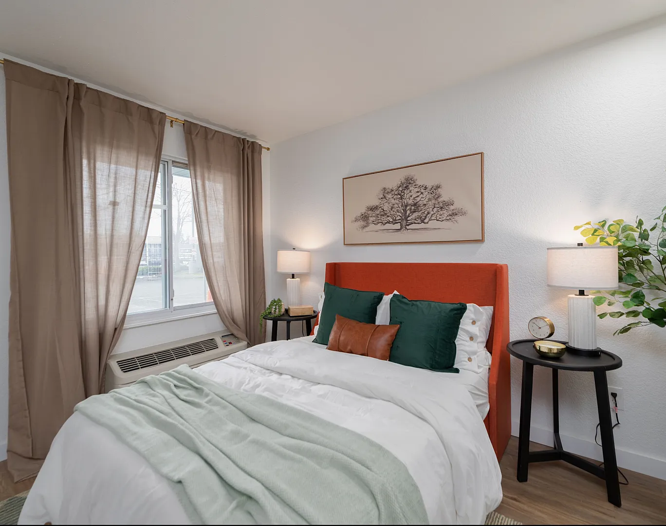 Bright and cozy bedroom with a modern orange headboard, soft green and white bedding, tasteful decor, and natural light from a window with elegant curtains.