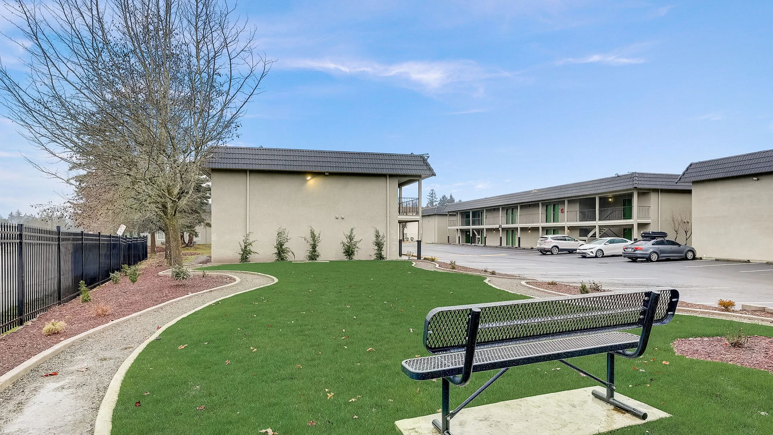 Serene apartment landscape featuring lush green lawn, tidy pathways, and a cozy bench, with modern buildings in the backdrop.