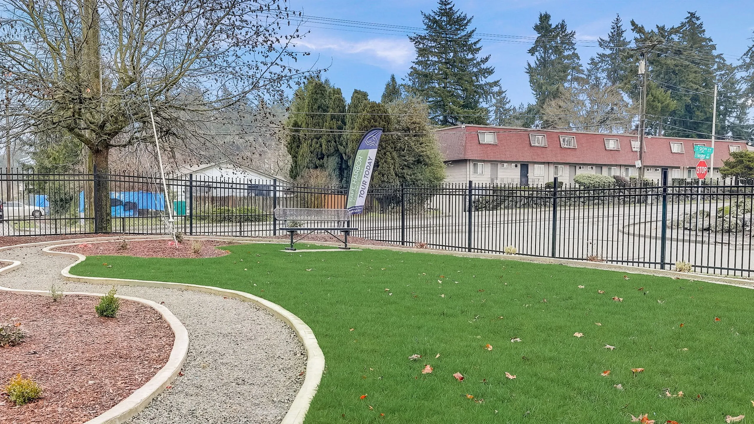 Charming garden area with a winding path, vibrant green grass, and a welcoming bench, surrounded by a stylish fence and mature trees.