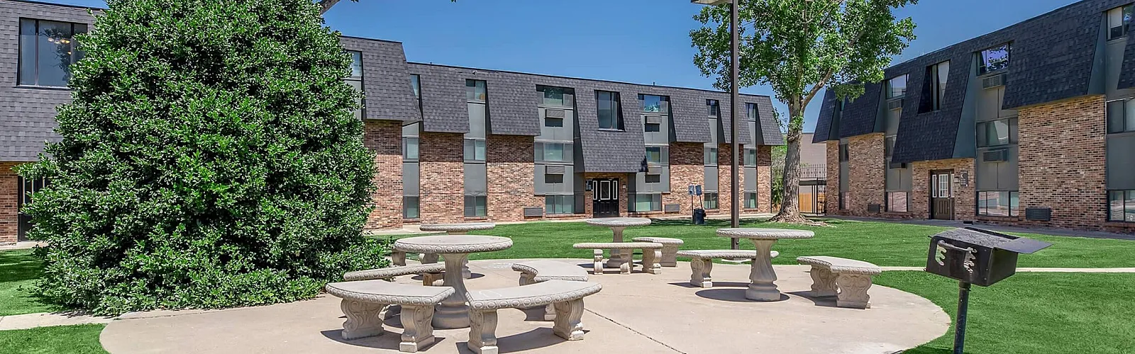 Inviting outdoor courtyard featuring stylish stone tables, lush green lawn, and modern apartment buildings in a vibrant community setting.