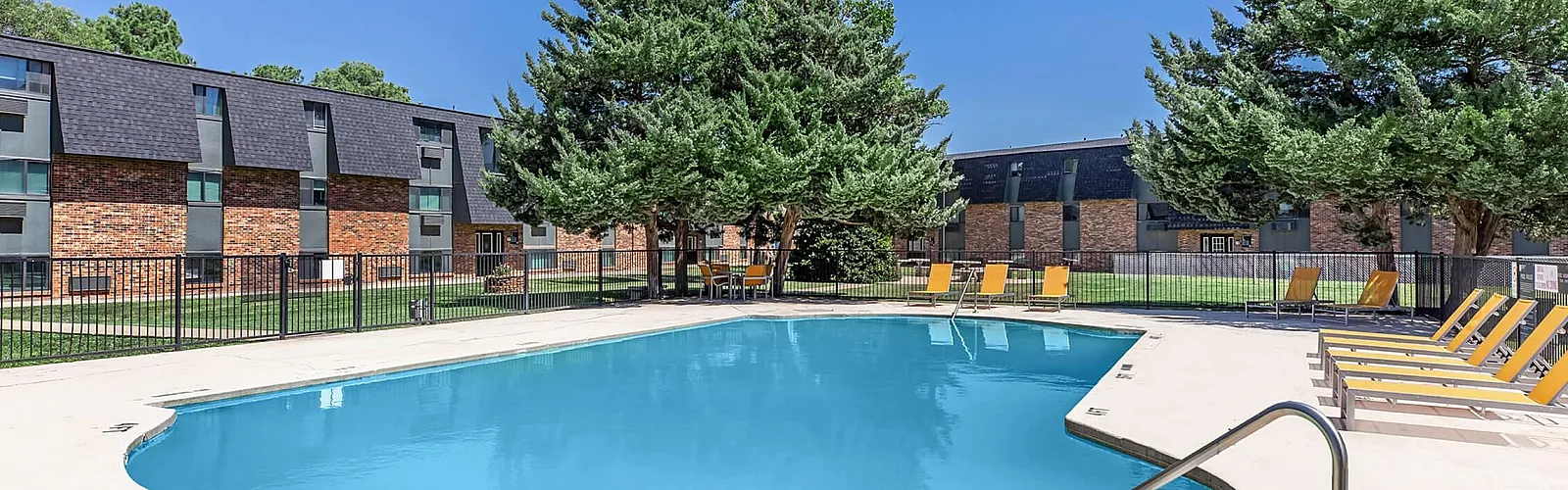 Inviting apartment complex with a sparkling outdoor pool surrounded by lush greenery and relaxing lounge chairs.