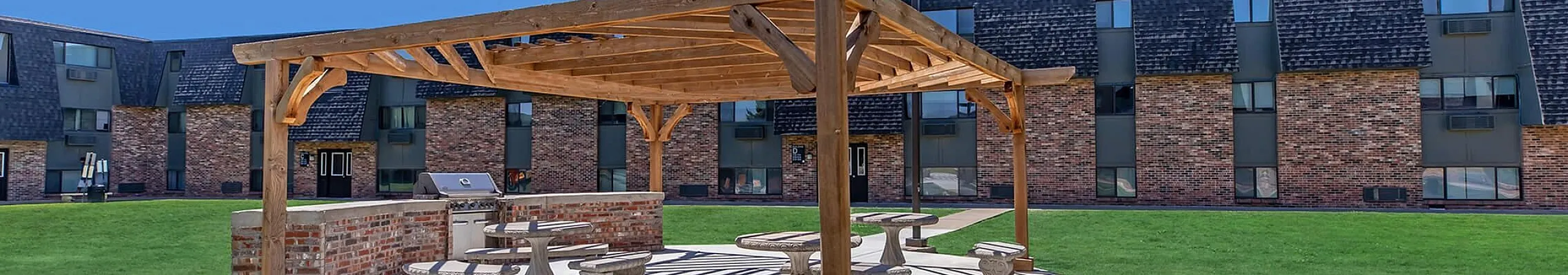 Charming outdoor space with a wooden pergola, picnic tables, and lush green lawn, perfect for relaxation and gatherings.
