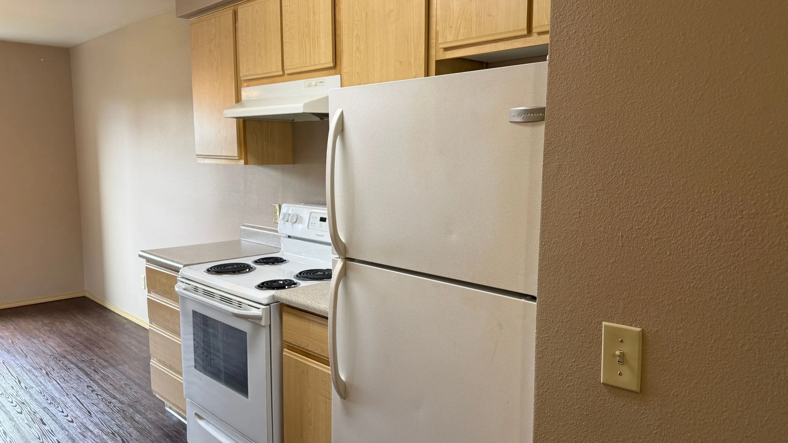 Cozy kitchen with modern wooden cabinetry, electric stove, and spacious refrigerator, accentuated by warm lighting.