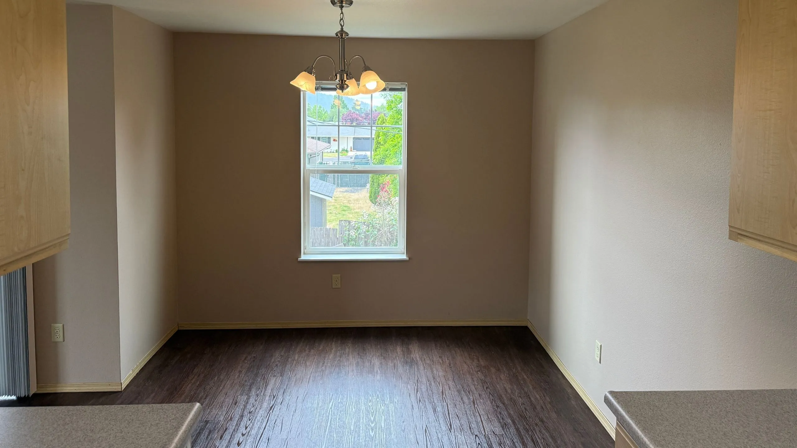 Bright dining area with elegant chandelier and large window overlooking a landscaped garden.