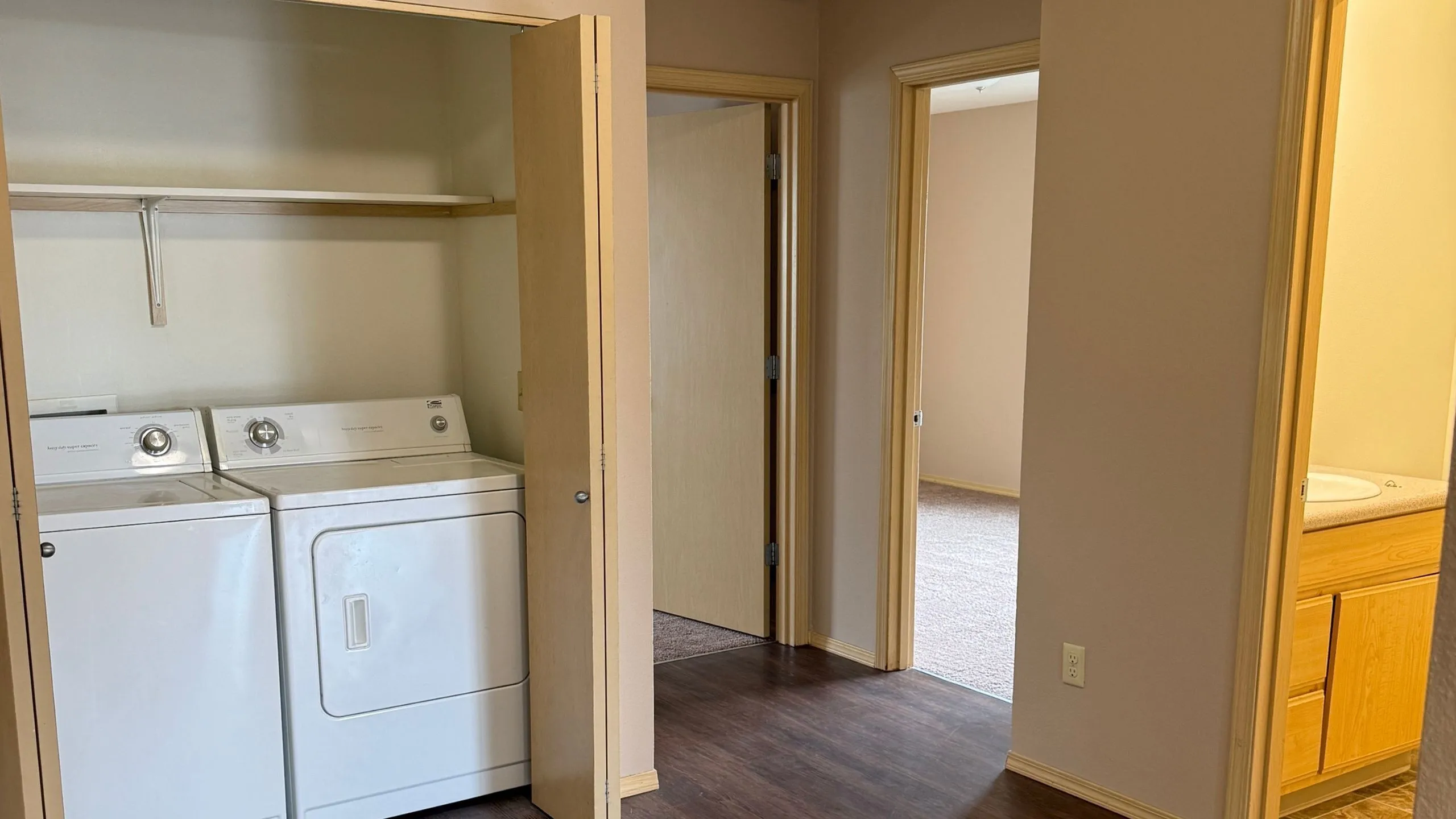 Convenient apartment hallway featuring in-unit washer and dryer, elegant wood flooring, and access to bedroom and bathroom.