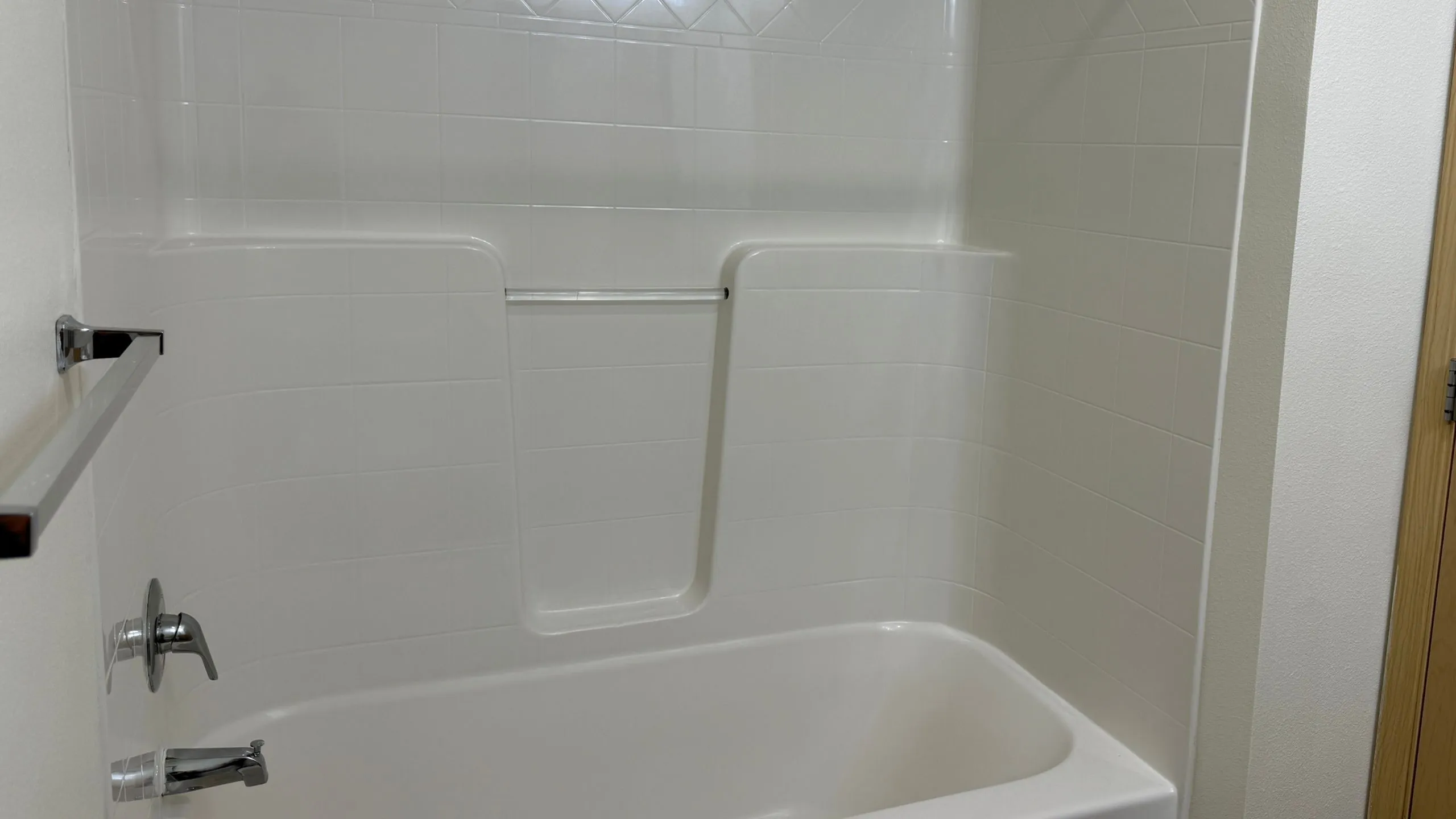 Elegant white tiled bathtub area with modern chrome fixtures, offering a clean and serene bathroom retreat.