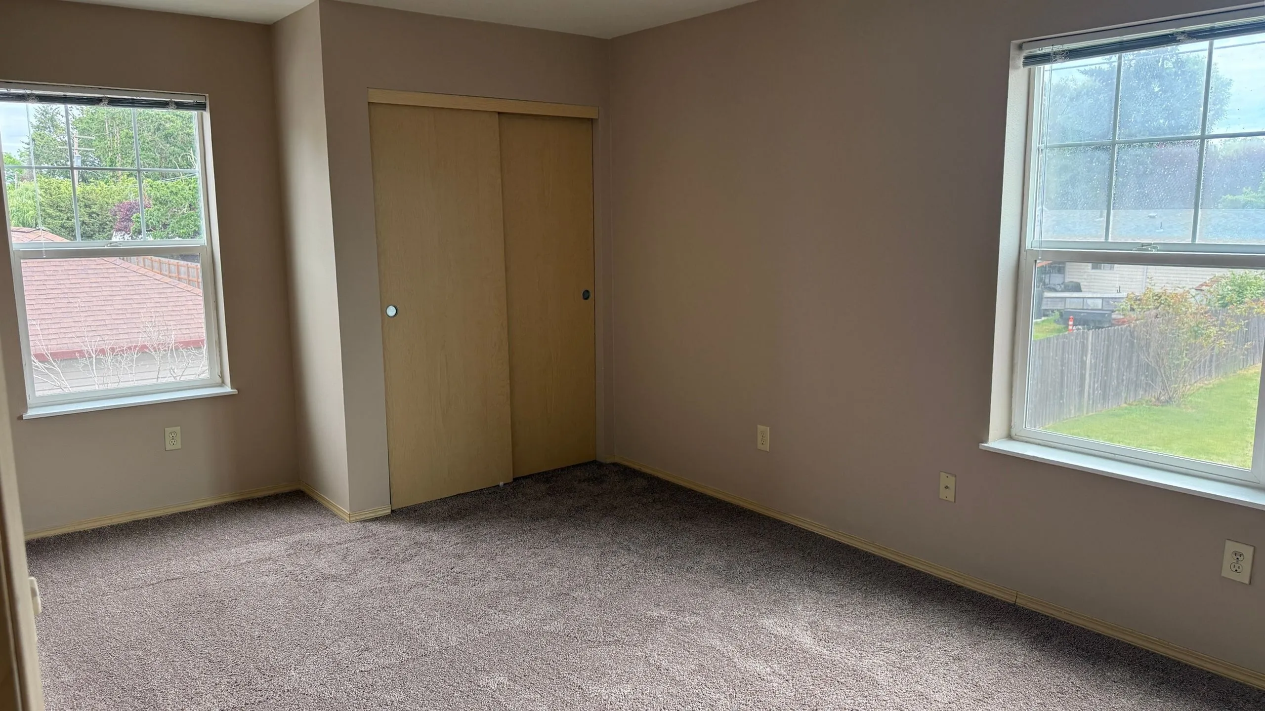 Bright and inviting bedroom with soft carpet, two large windows for natural light, and a spacious closet with wooden sliding doors.