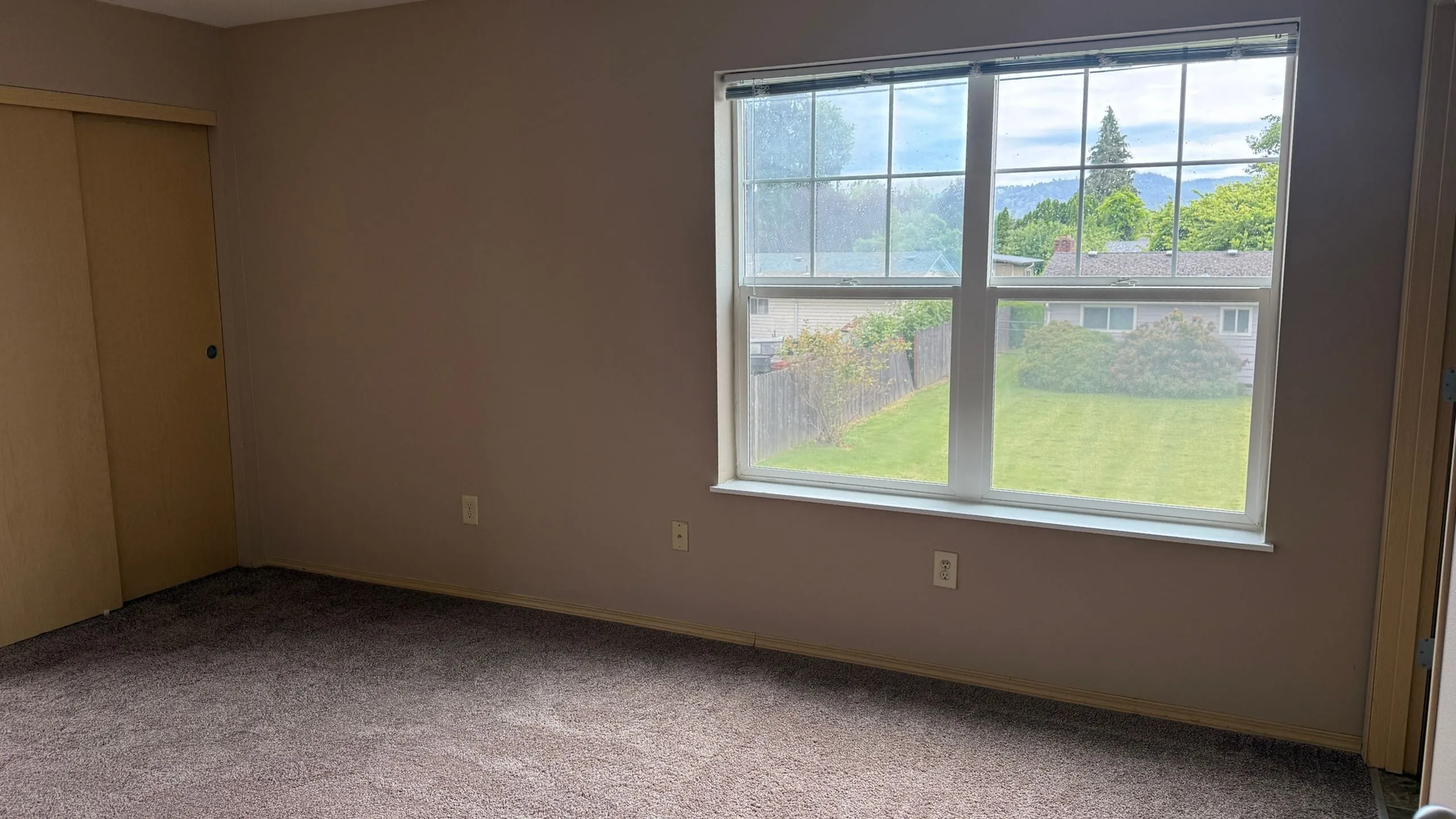 Bright bedroom with plush carpeting and a large window showcasing serene garden views.