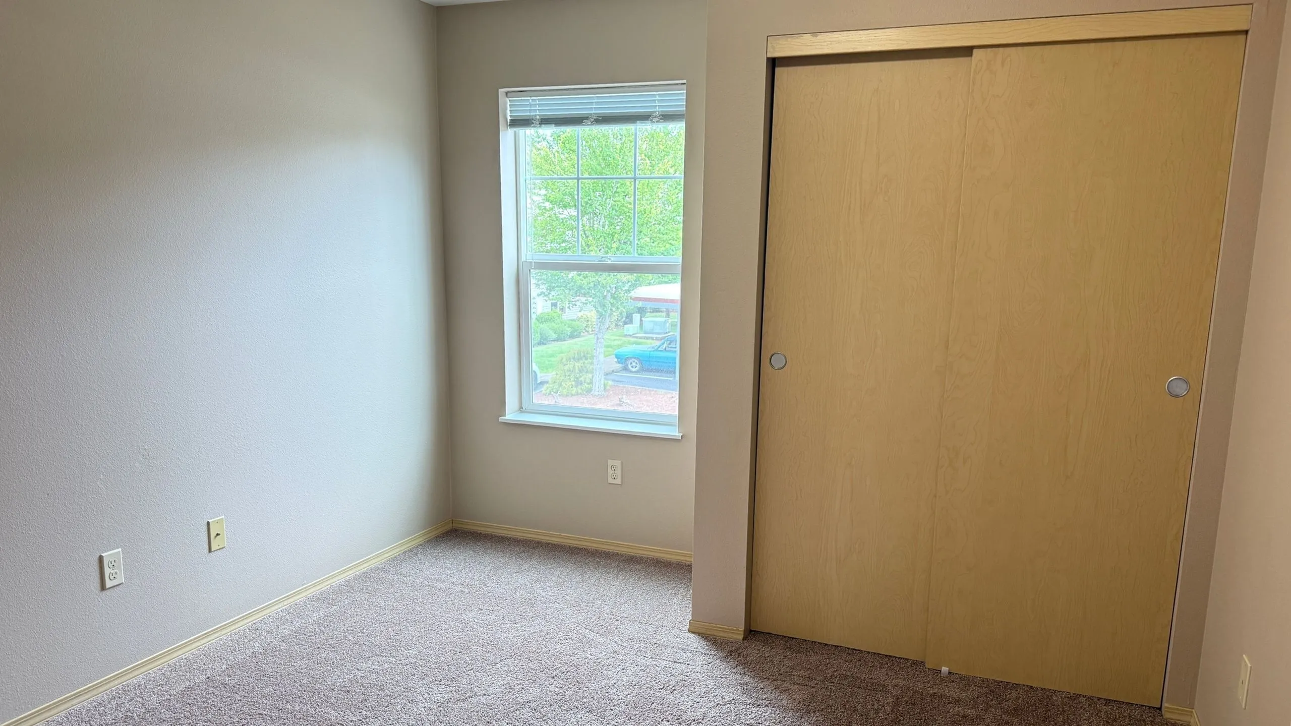 Inviting bedroom with soft carpet, large window for natural light, and a wooden sliding door closet.