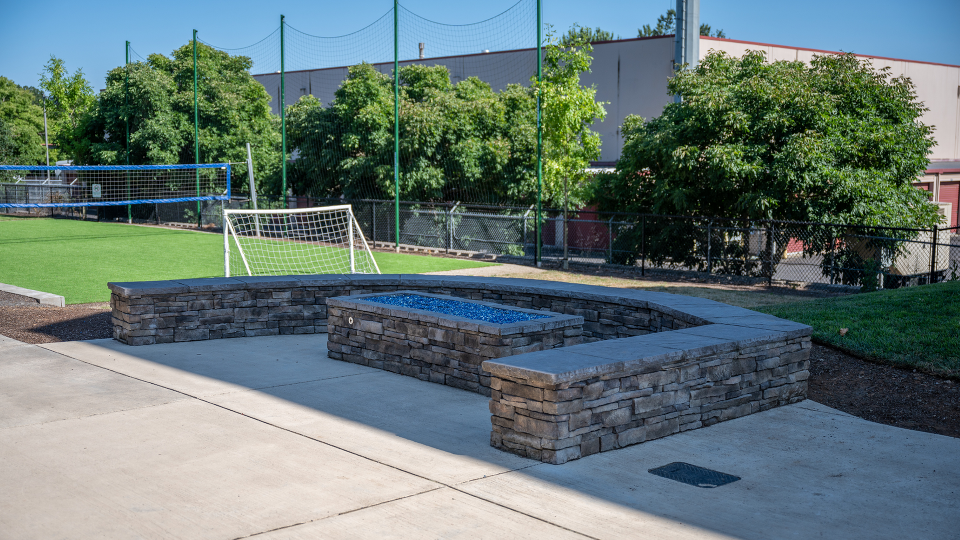 Inviting outdoor space with a stylish stone fire pit and green turf area, ideal for relaxation and recreation.