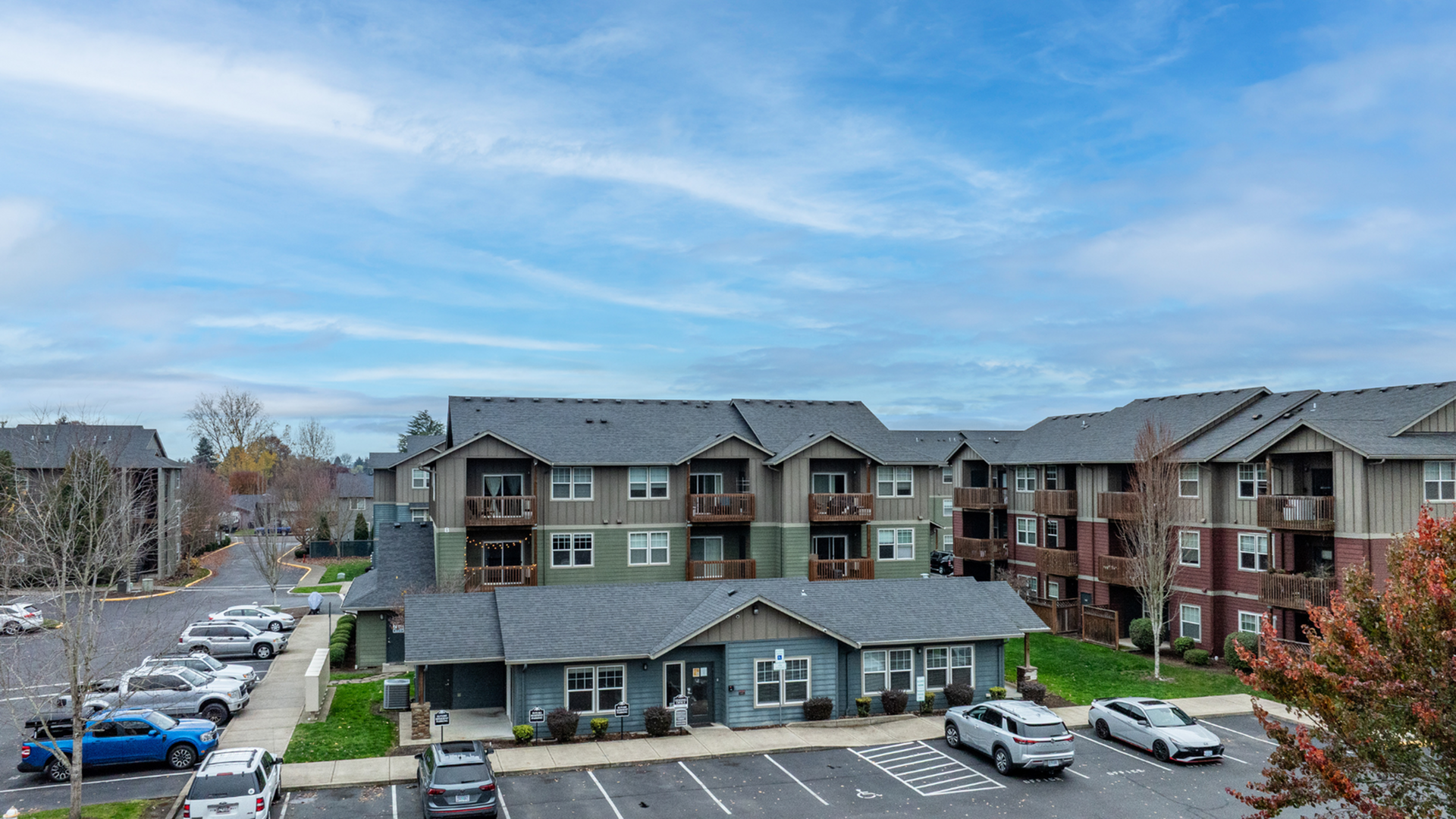 Charming apartment complex featuring balconies, ample parking, and beautiful landscaping under a clear sky.