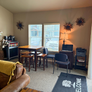 Cozy apartment corner featuring a stylish coffee station, a welcoming dining area, and ample natural light from large windows.
