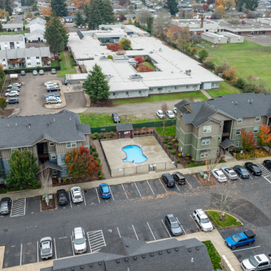 Inviting aerial view of a charming apartment complex with a community pool, neatly arranged parking, and lush greenery.