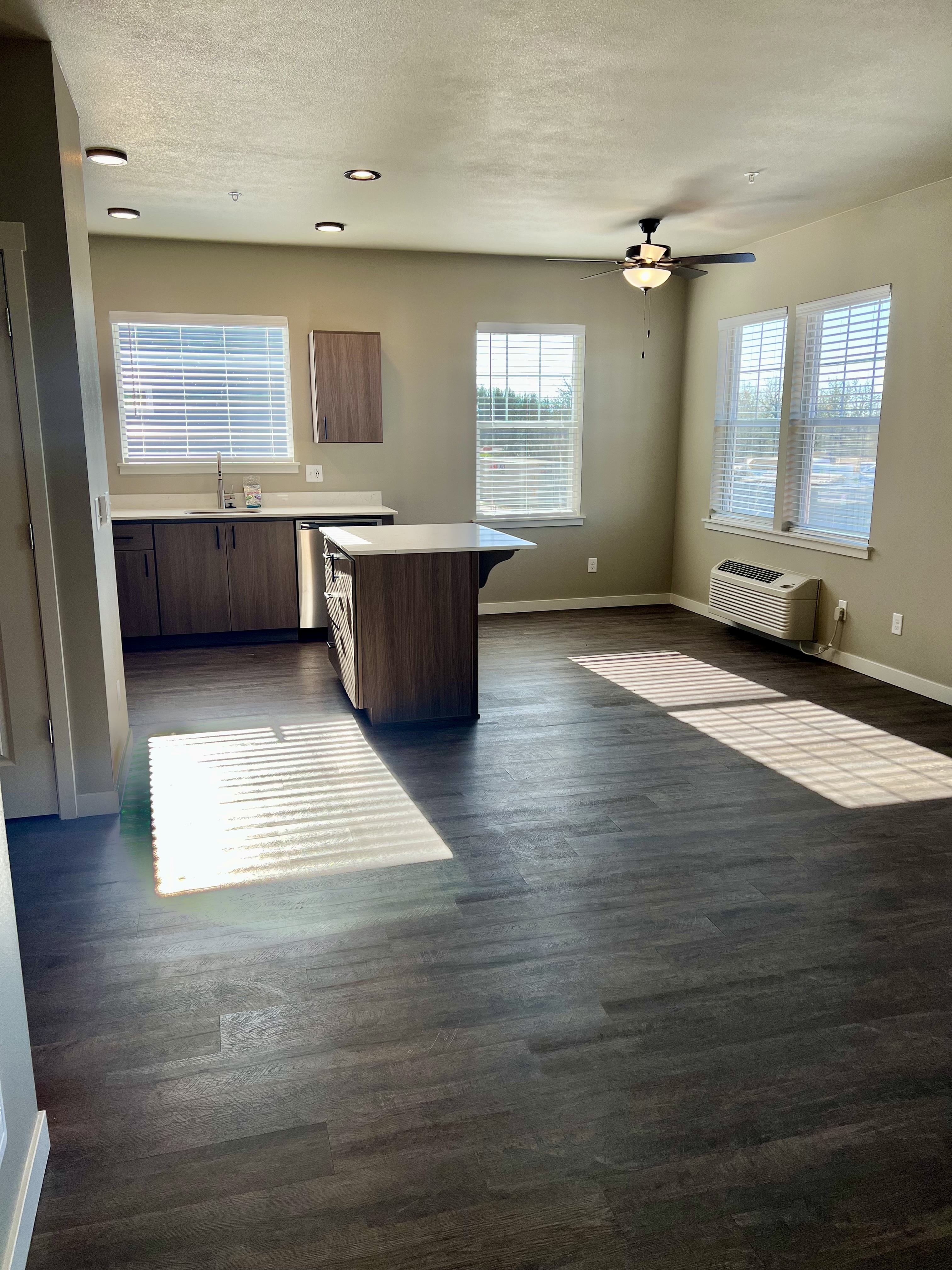 Bright open-plan living area with modern wood floors, kitchen island, and ample natural light from large windows.