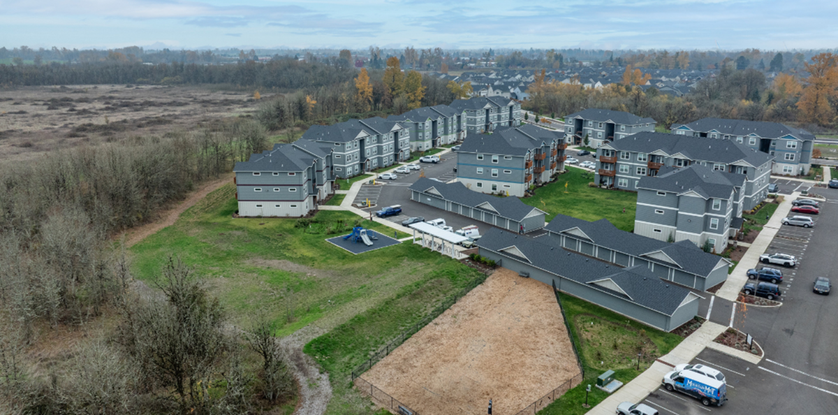 Aerial view of a modern apartment complex surrounded by lush greenery, featuring ample parking and a community playground.