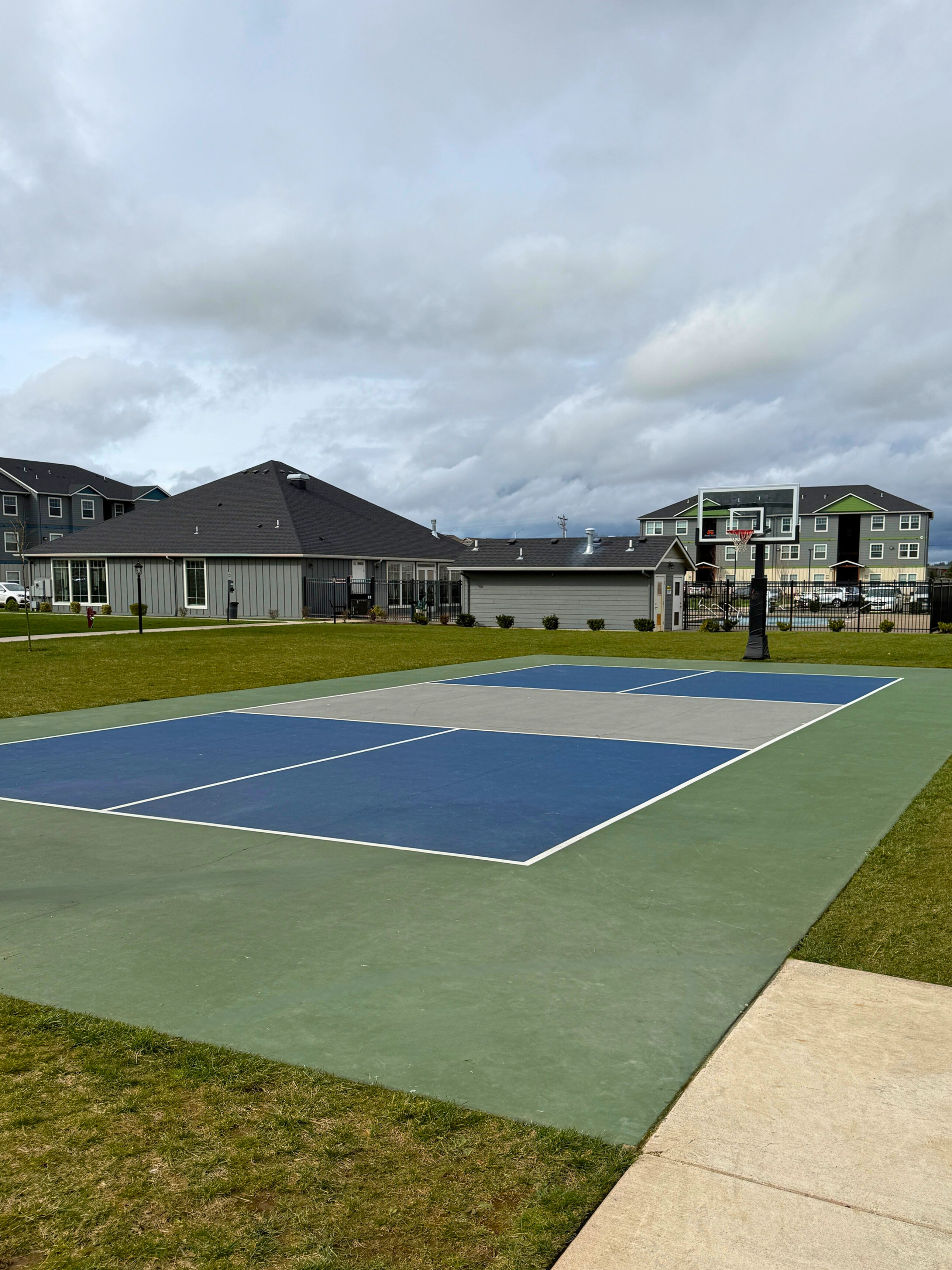Vibrant sports court in a modern community setting, featuring a sleek blue and green design with surrounding lush greenery and contemporary buildings.