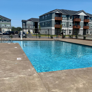 Inviting outdoor pool area with crystal clear water, surrounded by contemporary apartment buildings under a clear blue sky.