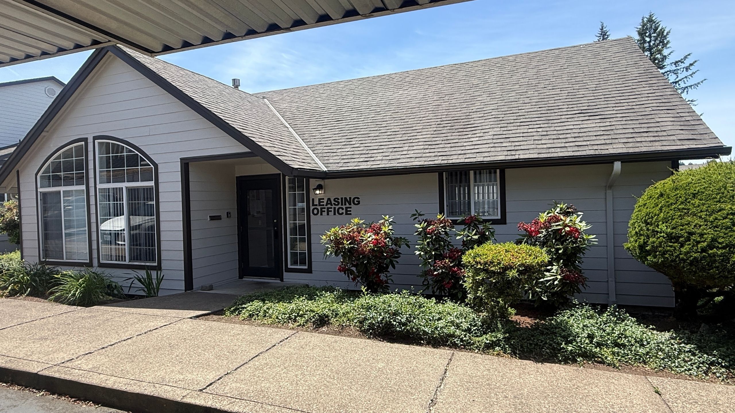 Charming leasing office with fresh landscaping and welcoming entrance under a sunny sky.
