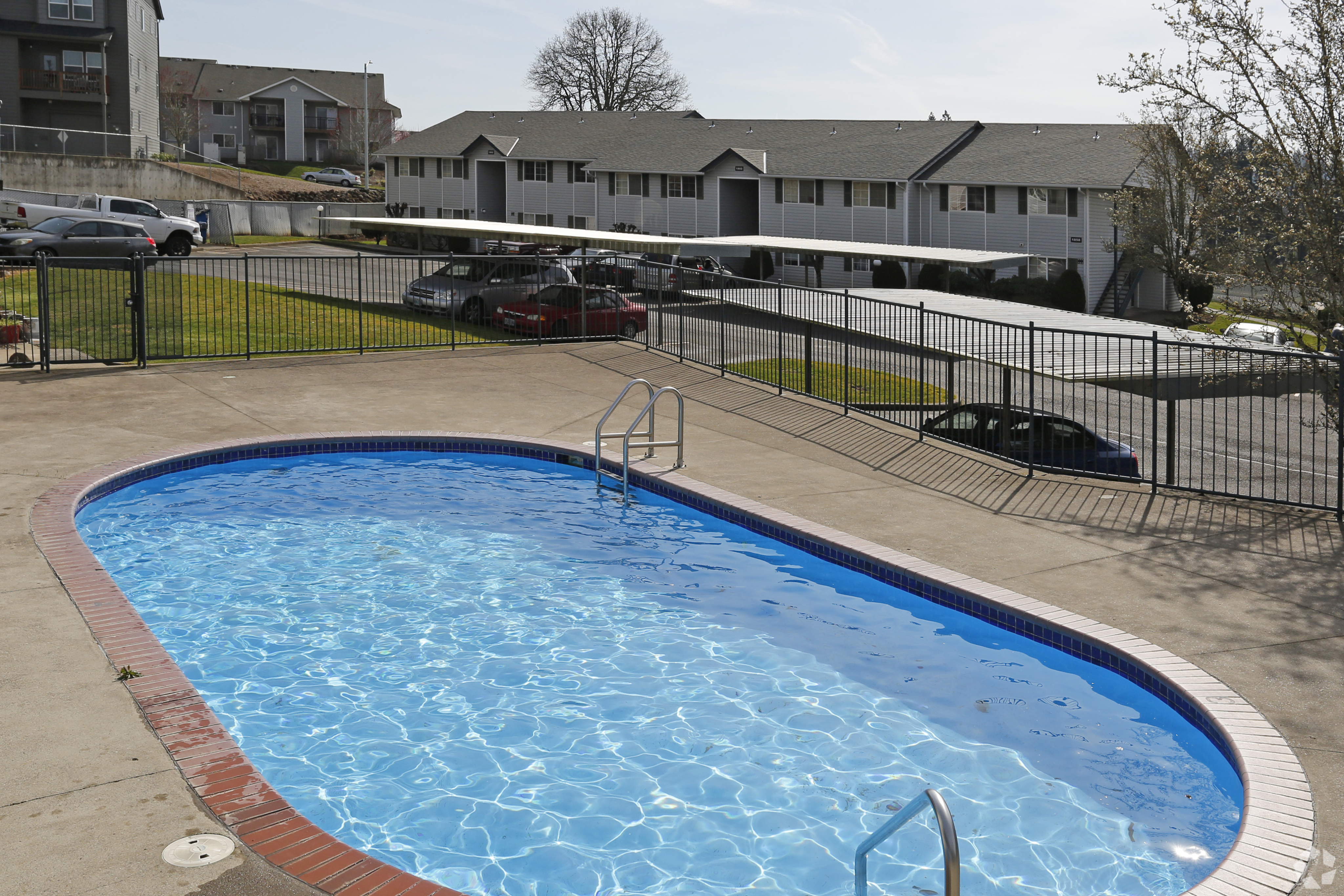 Inviting apartment complex surrounded by lush greenery, featuring a sparkling outdoor swimming pool with a modern gated entry.