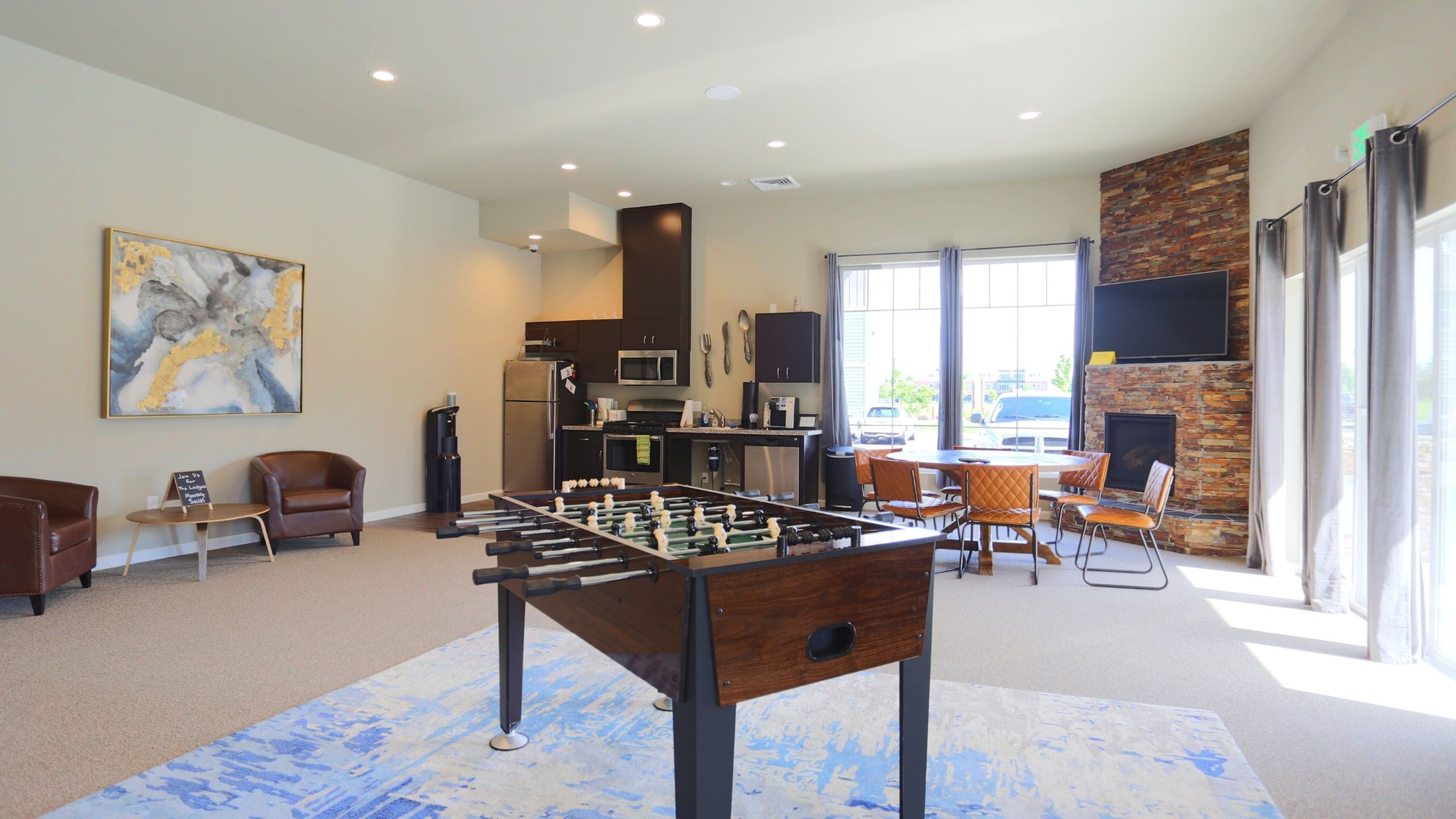 Inviting community lounge with foosball table, modern kitchenette, and cozy fireplace, perfect for entertainment and relaxation.