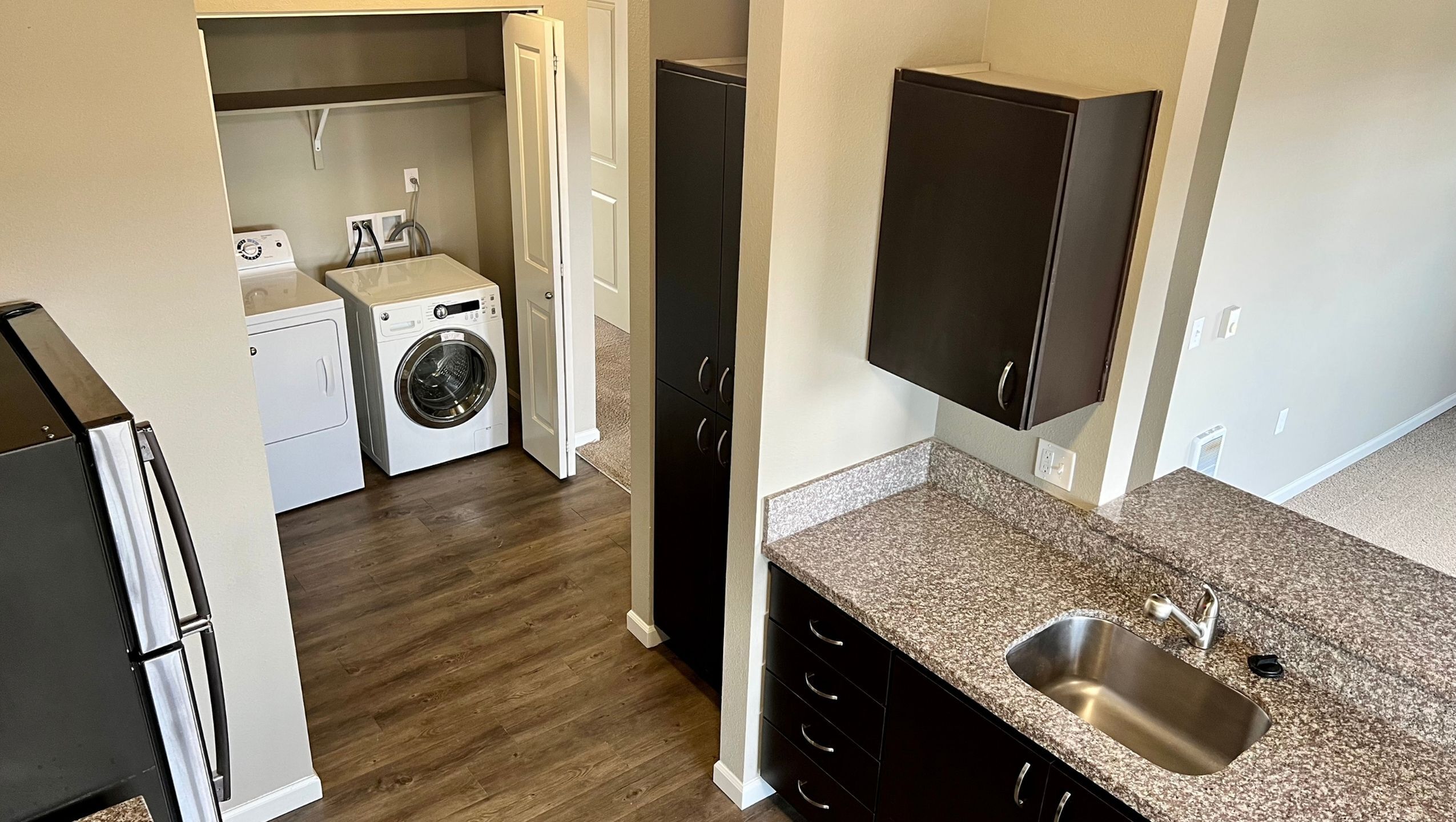 Contemporary apartment with sleek kitchen, modern appliances, and separate laundry area featuring a washer and dryer, all set on stylish wood flooring.