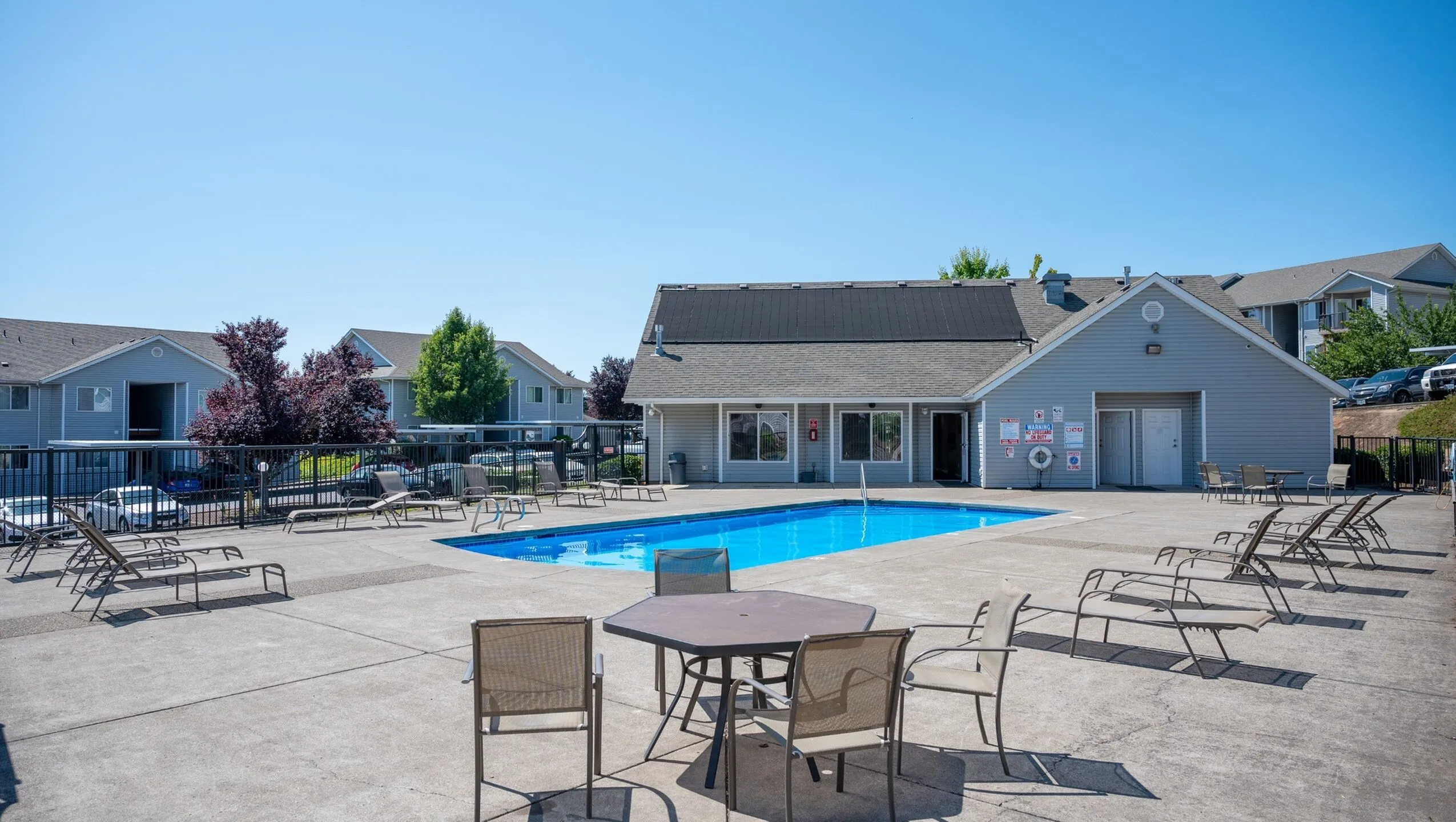 Inviting apartment complex with a sparkling swimming pool, spacious lounging area, and charming clubhouse, ideal for relaxation and community gatherings.