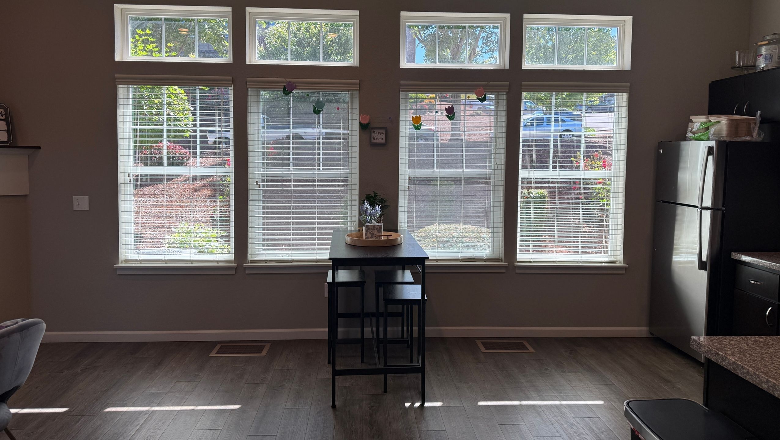 Bright modern kitchen and dining area with large windows, sleek stainless-steel appliances, and elegant wood flooring.