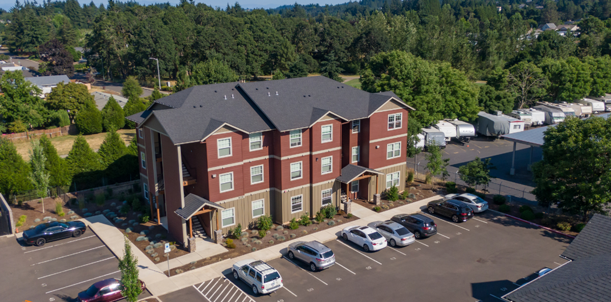 Charming red-brick apartment complex surrounded by lush greenery, featuring ample parking and a tranquil setting.