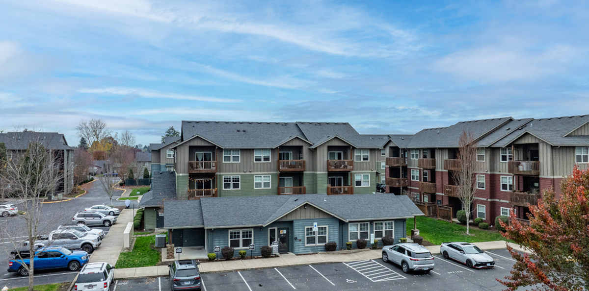 Scenic apartment complex with modern architecture, surrounded by lush greenery and ample parking space.