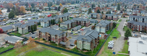 Charming aerial view of a modern apartment complex nestled in a lush suburban area, showcasing multi-story buildings surrounded by greenery, perfect for convenient and serene living.