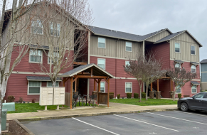 Charming three-story apartment building with a rustic, wood-paneled exterior and cozy entrance amidst lush landscaping.