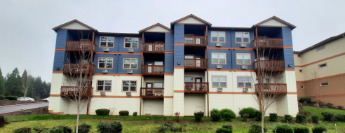 Charming multi-story apartment building with blue accents and inviting balconies, set amidst a lush green landscape.