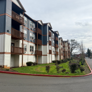 Charming multi-level apartment building with wooden balconies and manicured green lawn along a quiet street.
