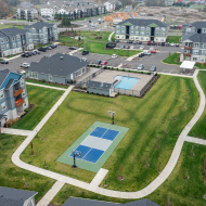 Aerial view of a vibrant apartment complex featuring lush green spaces, sports court, and inviting pool area within a welcoming community.
