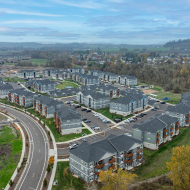Scenic aerial view of modern apartment complex surrounded by lush greenery and winding roads, offering a serene living environment.