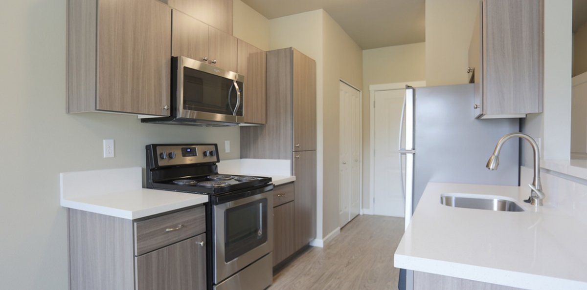 Modern kitchen with sleek stainless steel appliances, elegant wood cabinetry, and pristine white countertops, offering a stylish and functional cooking space.
