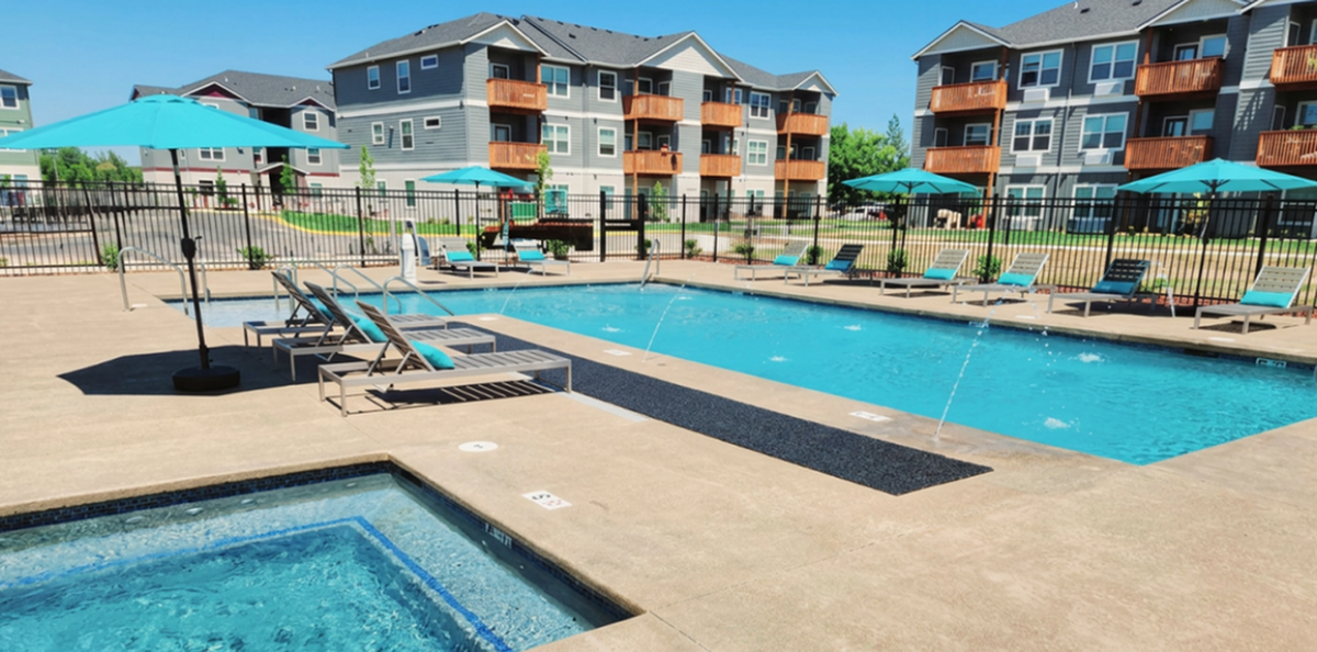 Inviting apartment complex with a sparkling outdoor pool, elegant sun loungers, and vibrant blue umbrellas, offering a perfect spot for relaxation and leisure.