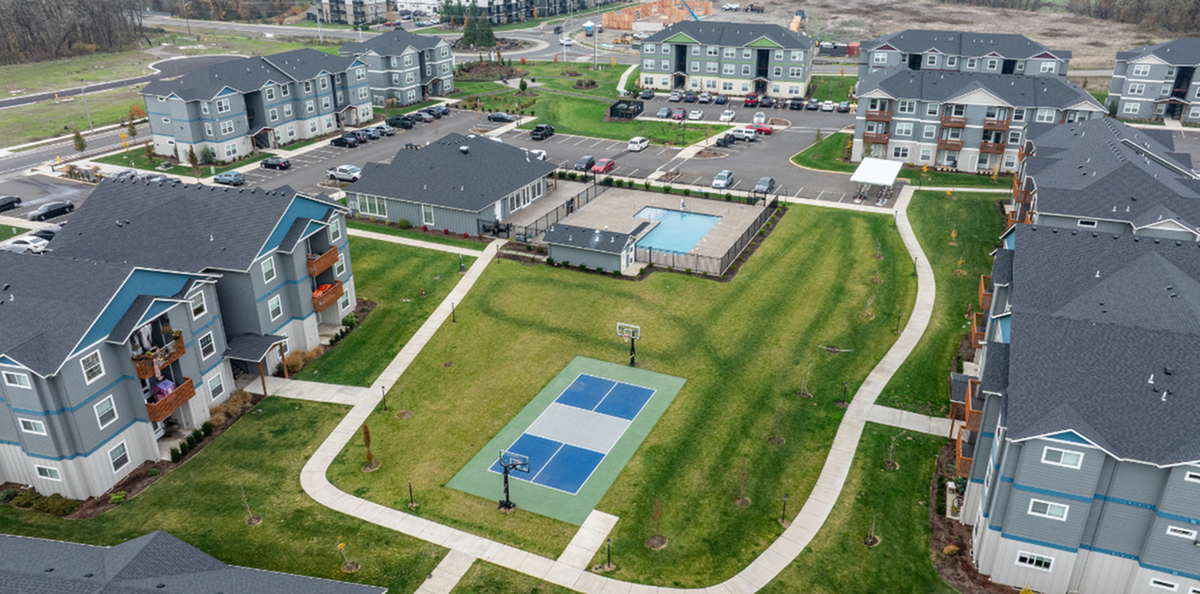 Aerial view of a modern apartment complex featuring landscaped green spaces, a community swimming pool, and a basketball court, providing a vibrant and inviting residential environment.
