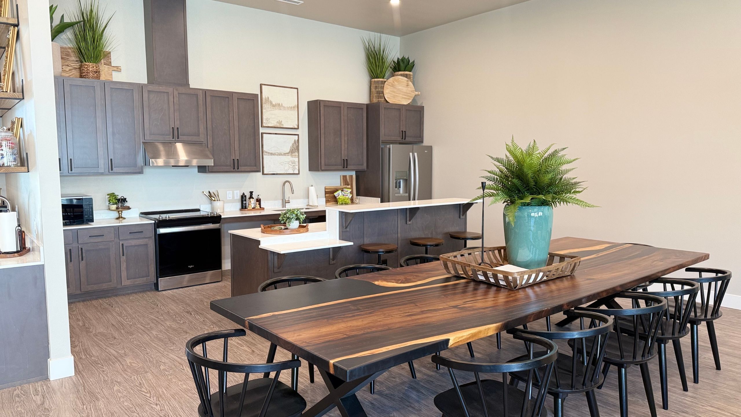 Modern open-concept kitchen and dining area featuring sleek dark cabinets, stainless steel appliances, and a stunning wooden dining table with ample seating.